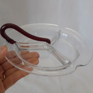 May include: A clear glass divided serving dish with a red glass handle. The dish has three sections.