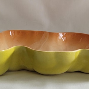 May include: A ceramic serving dish with a unique, three-sectioned design. The exterior is a vibrant yellow-green, while the interior transitions from a warm orange to a lighter peach color. This decorative dish is ideal for serving snacks or displaying decorative items.