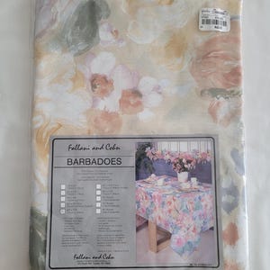 May include: A floral tablecloth in a plastic package. The tablecloth features a pattern of pink, peach, and white flowers on a light beige background. The label reads "Fallani and Cohn BARBADOES".