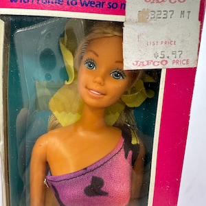 Puede incluir: Muñeca vintage en su embalaje original. La muñeca tiene cabello rubio, ojos azules y viste un top morado y negro. El embalaje incluye el texto "FOR AGES OVER 3" y una etiqueta de precio.