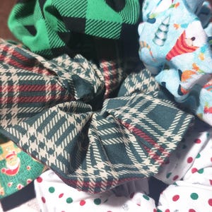 May include: A collection of five fabric scrunchies in various holiday patterns. The scrunchies are made of green, red, white, and blue fabrics. The patterns include plaid, polka dots, and a Christmas-themed design.