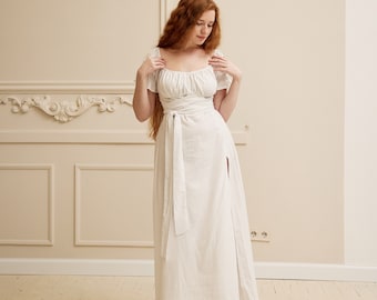 May include: A white maxi dress with a square neckline, short sleeves, and a tie at the waist. The dress has a thigh-high slit on one side.