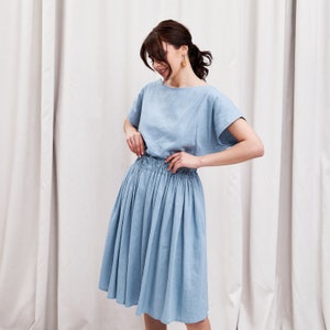 May include: A light blue linen dress with a gathered skirt and short sleeves. The dress has a relaxed fit and a casual style.