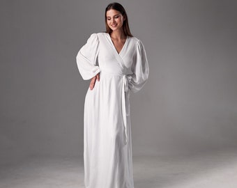 May include: A white wrap dress with long sleeves and a cinched waist. The dress is made of a soft, flowing fabric and has a relaxed fit.