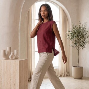 May include: A sleeveless, deep burgundy top with a round neckline and side slits, paired with light beige trousers. The top features a straight hemline that is slightly longer in the back, creating a relaxed silhouette with clean, simple lines.