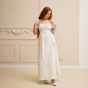 May include: A white maxi dress with a square neckline, short sleeves, and a tie at the waist. The dress has a thigh-high slit on the right side.