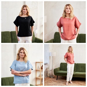 May include: Three women are wearing different colored linen tops. The tops have a relaxed fit and short sleeves. The women are wearing white pants and are standing in front of a green sofa.