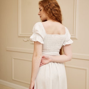 May include: A white linen dress with a square neckline and short puff sleeves. The dress has a fitted bodice and a flowing skirt.