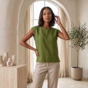 May include: A sleeveless olive green top with a round neckline and a straight hemline, paired with light beige trousers. The top features a simple, clean-cut design with wide shoulder coverage and a relaxed fit, crafted from a solid-colored fabric.