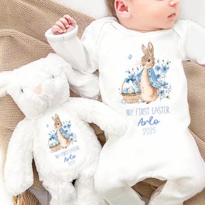 May include: White baby onesie with a blue and brown bunny rabbit holding a basket of Easter eggs. The onesie says "My First Easter Arlo 2025". A white plush bunny with the same design is next to the onesie.