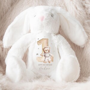 May include: White plush bunny with a brown number one and a bear astronaut design. The bunny has a personalized message that says "Happy First Birthday Hudson".