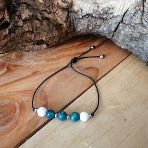 Puede incluir: Un brazalete de cuerda negra con cuentas turquesa y blancas. El brazalete es ajustable con un nudo deslizante.