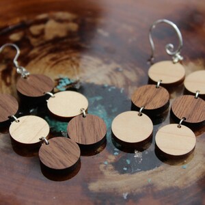 May include: A pair of wooden earrings with a silver hook. The earrings are made of alternating light and dark wood circles.