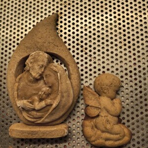 May include: A light brown, textured, molded cookie shaped like a teardrop containing a relief of a family unit with two adults and a child, alongside a separate light brown, textured, molded cookie shaped like a small angel with wings.