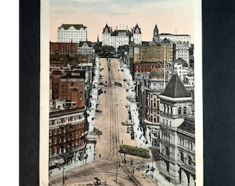 May include: A vintage postcard depicting a view of State Street in Albany, New York, looking up from the D. & H. Building. The street is lined with buildings, including the Hampton Hotel, and features streetcars and pedestrians.