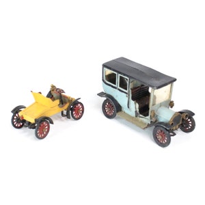 May include: Two vintage toy cars, one yellow with a black top and the other blue with a black top. Both cars have black wheels with red accents.