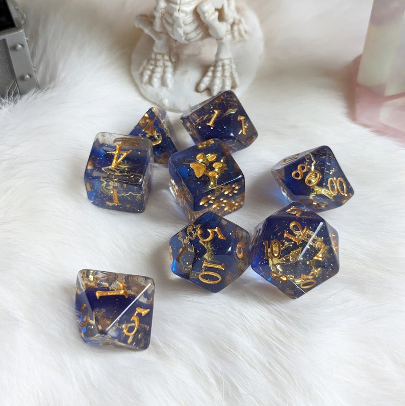 May include: A set of seven blue and gold dice with gold glitter embedded in the resin. The dice are numbered 1-6, 8, 10, and 12.
