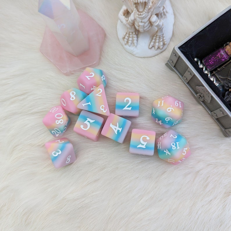 May include: A set of ten colorful dice with rainbow-colored swirls and white numbers. The dice are made of a soft, squishy material.