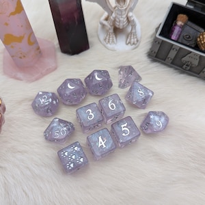 May include: A set of 10 purple dice with silver glitter and white numbers. The dice are in a variety of shapes, including a d4, d6, d8, d10, d12, and d20.