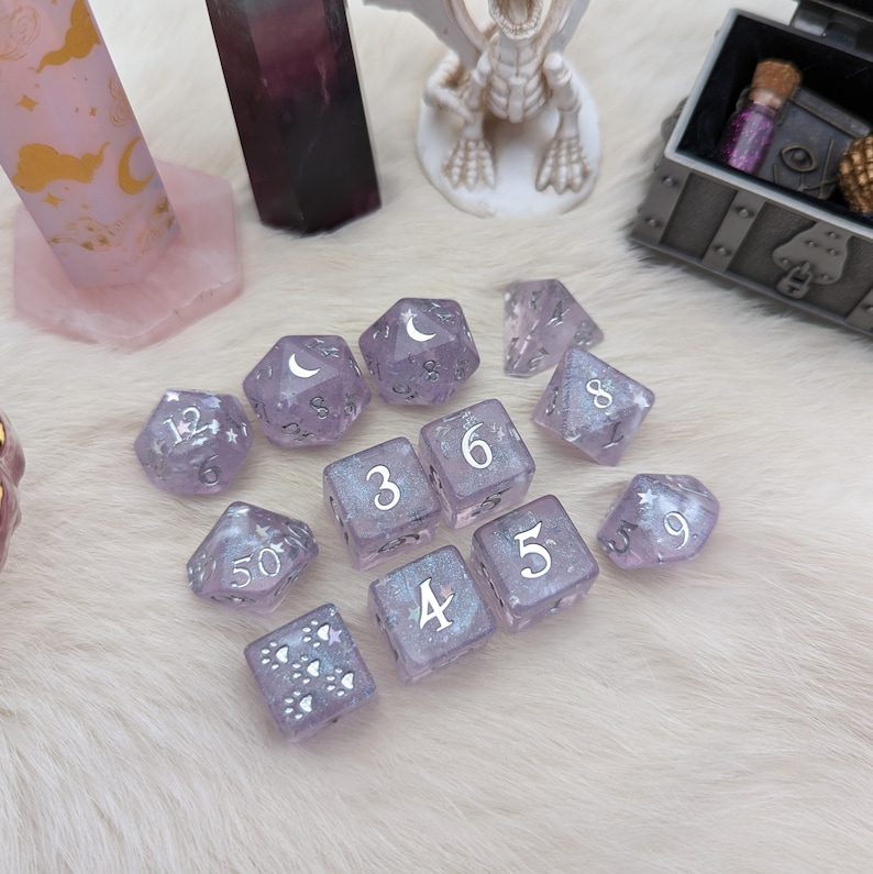 May include: A set of 10 purple dice with silver glitter and white numbers. The dice are in a variety of shapes, including a d4, d6, d8, d10, d12, and d20.