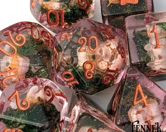 May include: Set of pink and clear dice with copper numbers and floral accents. The dice are filled with glitter and have a mossy green background.