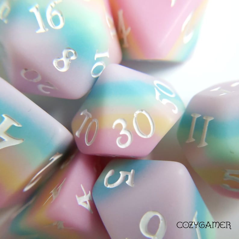 May include: A set of pastel-colored dice with white numbers. The dice are made of a translucent material and have a rainbow swirl pattern. The numbers on the dice are 1, 2, 3, 4, 5, 6, 8, 10, 16, 20, and 30.