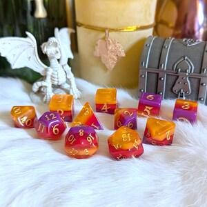 May include: A collection of colorful, resin dice in shades of orange, purple, and red. The dice are of various shapes, including a pyramid and a 20-sided die. A small, decorative treasure chest and a white dragon figurine are in the background.