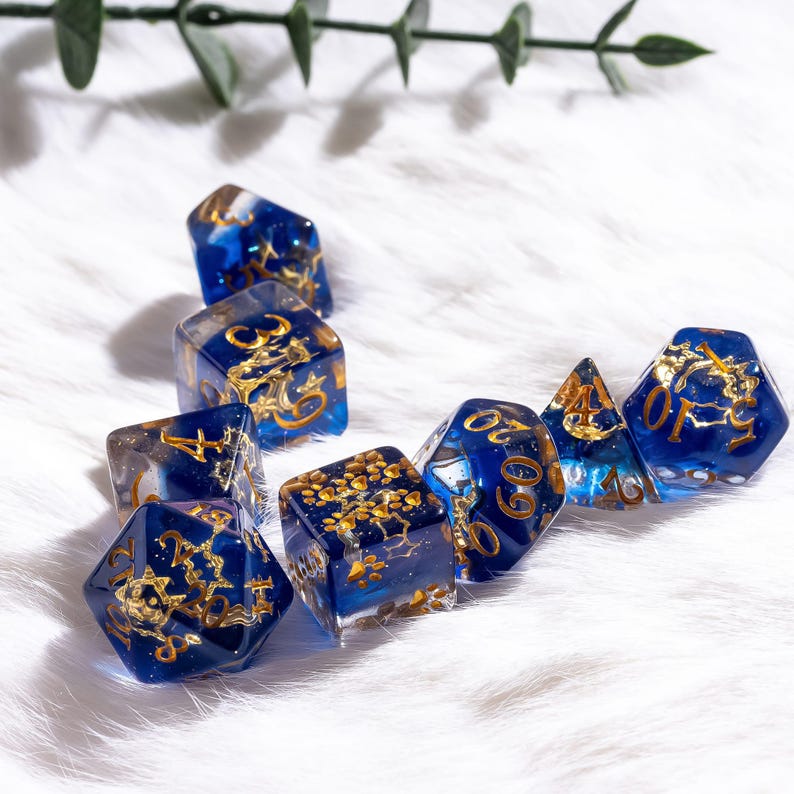 May include: Set of eight polyhedral dice in various shapes. The dice are a deep blue with gold-colored numbers and decorative elements. The dice are arranged on a white, fluffy surface.