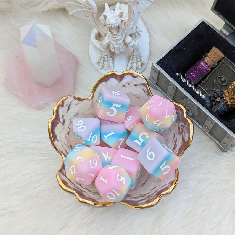 May include: A collection of pastel-colored dice with white numbers in a decorative bowl. The dice are a mix of pink, blue, and yellow.