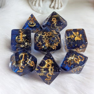 May include: Set of eight blue and gold dice with various symbols and numbers. The dice are made of clear resin with gold glitter and gold paint.