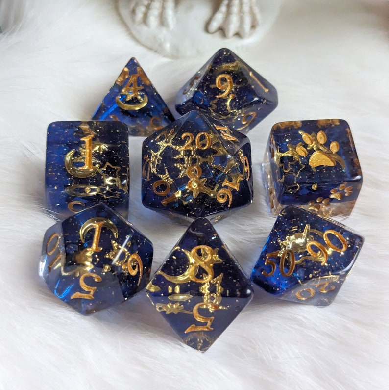 May include: Set of eight blue and gold dice with various symbols and numbers. The dice are made of clear resin with gold glitter and gold paint.