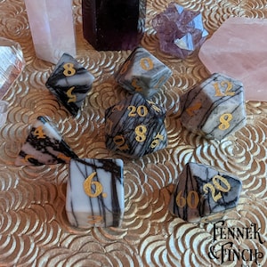 May include: Set of seven black and white marble dice with gold numbers. The dice are on a gold background with a pattern of overlapping circles.