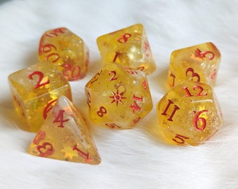 May include: Set of seven translucent yellow dice with red numbers. The dice are speckled with gold glitter and have a variety of shapes and sizes.
