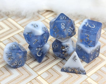 May include: A set of seven blue and white dice with silver numbers and gold flecks. The dice are a d4, d6, d8, d10, d12, and d20.