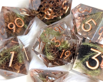 May include: A set of seven polyhedral dice. Each die is clear with copper-colored numbers and filled with natural elements like pinecones and greenery. The dice are designed for tabletop games.