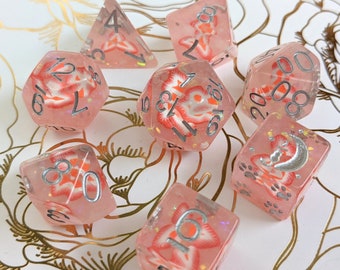 May include: A set of seven pink and white dice with silver numbers and a floral design. The dice are made of clear plastic with glitter embedded in the plastic. The dice are arranged in a circle on a white background with gold floral designs.