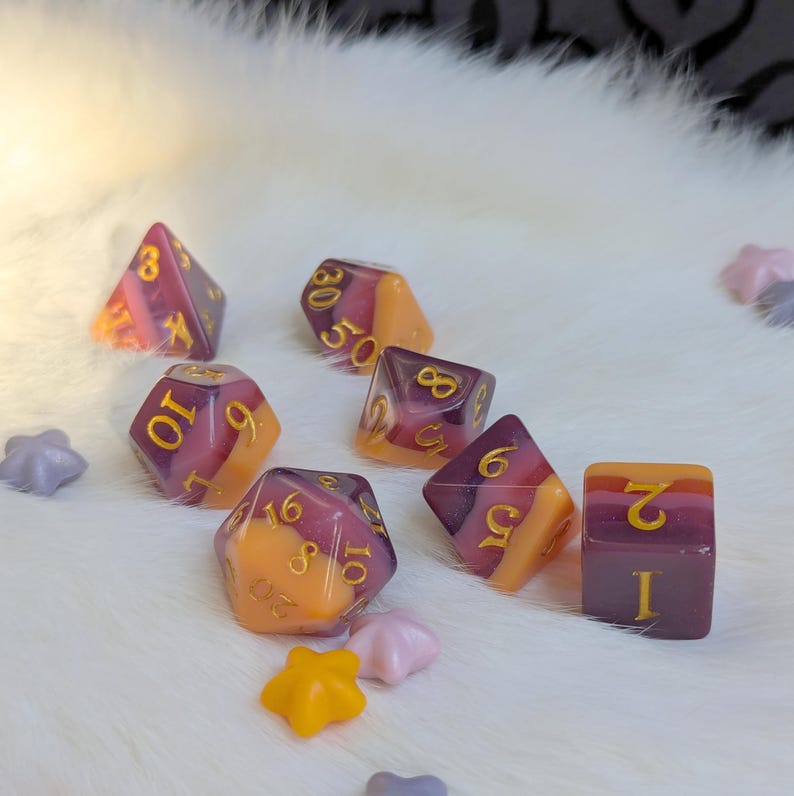 May include: Set of seven dice with a purple, orange, and yellow swirl pattern. The dice are numbered 1 through 10 and have gold numbers.