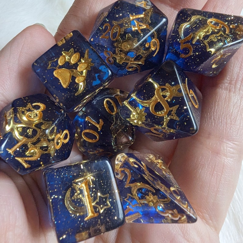 May include: A set of seven blue and gold dice with various symbols and numbers. The dice are made of a clear material with gold glitter embedded in it.
