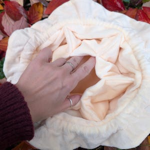 May include: A cream-colored, plush drawstring bag with a soft, quilted texture. The interior is a lighter shade of cream. The bag is open, revealing the inside. The image is taken from a top-down perspective.