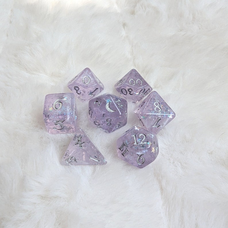 May include: Set of seven purple dice with silver glitter and white numbers. The dice are shaped like a traditional cube and have a variety of numbers on each side.
