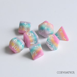 May include: Set of six iridescent dice with a rainbow swirl pattern. The dice are made of a translucent plastic and have white numbers. The dice are in a variety of shapes, including a d4, d6, d8, d10, d12, and d20.