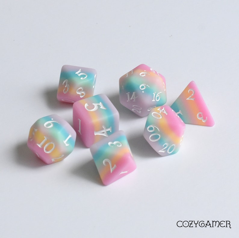 May include: Set of six iridescent dice with a rainbow swirl pattern. The dice are made of a translucent plastic and have white numbers. The dice are in a variety of shapes, including a d4, d6, d8, d10, d12, and d20.
