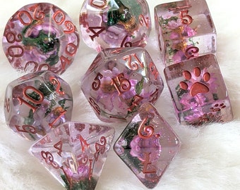 May include: Set of ten pink and clear dice with copper numbers and floral accents. The dice are translucent and show the flowers inside. The dice are numbered 1 through 10.