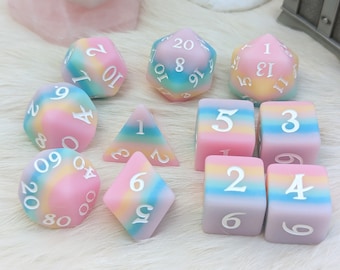 Puede incluir: Un conjunto de diez dados de múltiples caras en colores pastel. Los dados presentan una mezcla de rosa, azul, amarillo y morado, con números blancos. El conjunto incluye varias formas, como un d20, d12, d10, d8, d6 y d4.