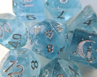 May include: A collection of light blue, gemstone-like dice with silver numbering. One die features a paw print design. The dice are in various shapes, including a d20, d12, and d6, and are ideal for tabletop games.