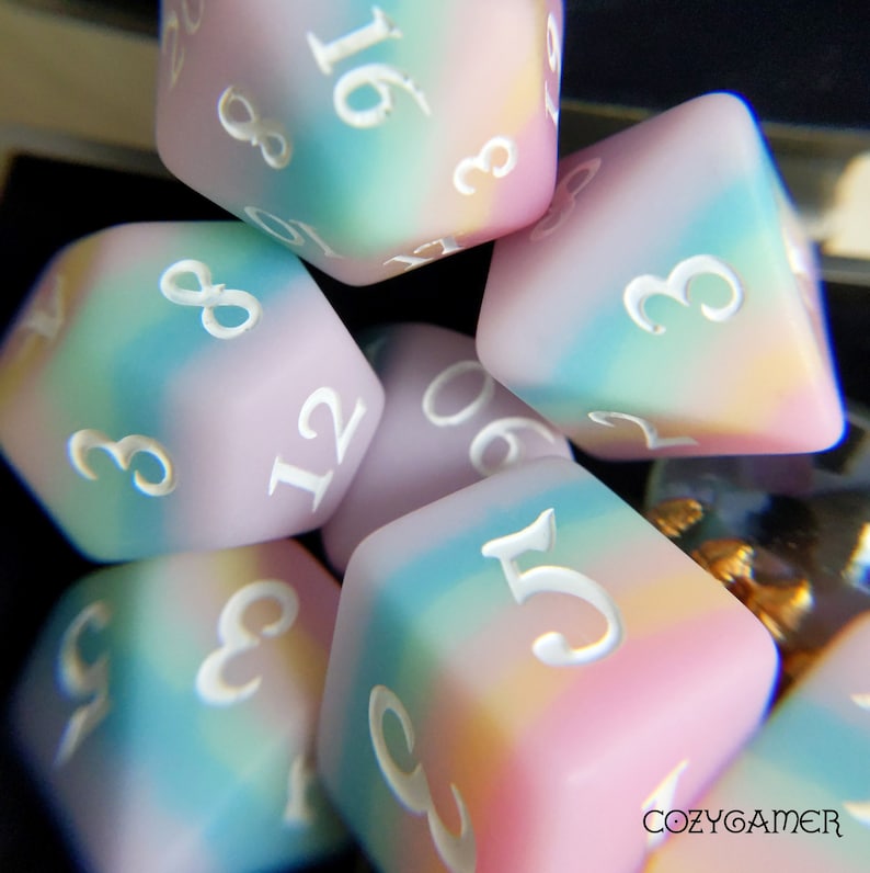 May include: A set of six pastel-colored dice with white numbers. The dice are made of a soft, translucent material and have a cloudy, marbled appearance. The numbers on the dice are 3, 5, 6, 8, 12, and 16.
