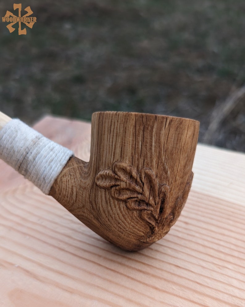 Pu&ograve; includere: Una pipa da fumo in legno con un design a foglia scolpito. La pipa &egrave; realizzata in legno marrone chiaro e ha una fascia bianca attorno al gambo.