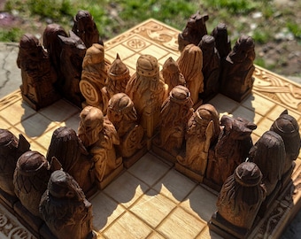 May include: A wooden chess set with Norse mythology figures. The pieces are carved in detail and are arranged on a wooden board with a Celtic knot design.