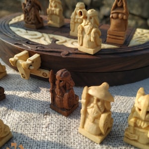 Puede incluir: Juego de mesa de madera con piezas talladas. Las piezas, en tonos marrones y beige, representan figuras con detalles. El tablero, marr&oacute;n oscuro, tiene incrustaciones claras, creando un contraste visual.