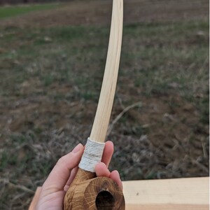 Pu&ograve; includere: Una pipa da fumo in legno con un lungo stelo curvo. La pipa &egrave; realizzata in legno marrone chiaro e ha una corda bianca avvolta attorno allo stelo vicino al fornello.